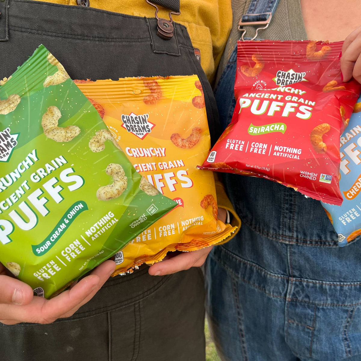 Two people holding one red bag of Sriracha Puffs, one blue bag of Cheddar Puffs, one yellow bag of Barbeque Puffs and one green bag of Sour Cream &amp; Onion Puffs 0.7oz.